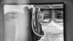 A grayscale capture of a woman wearing googles and PPE.